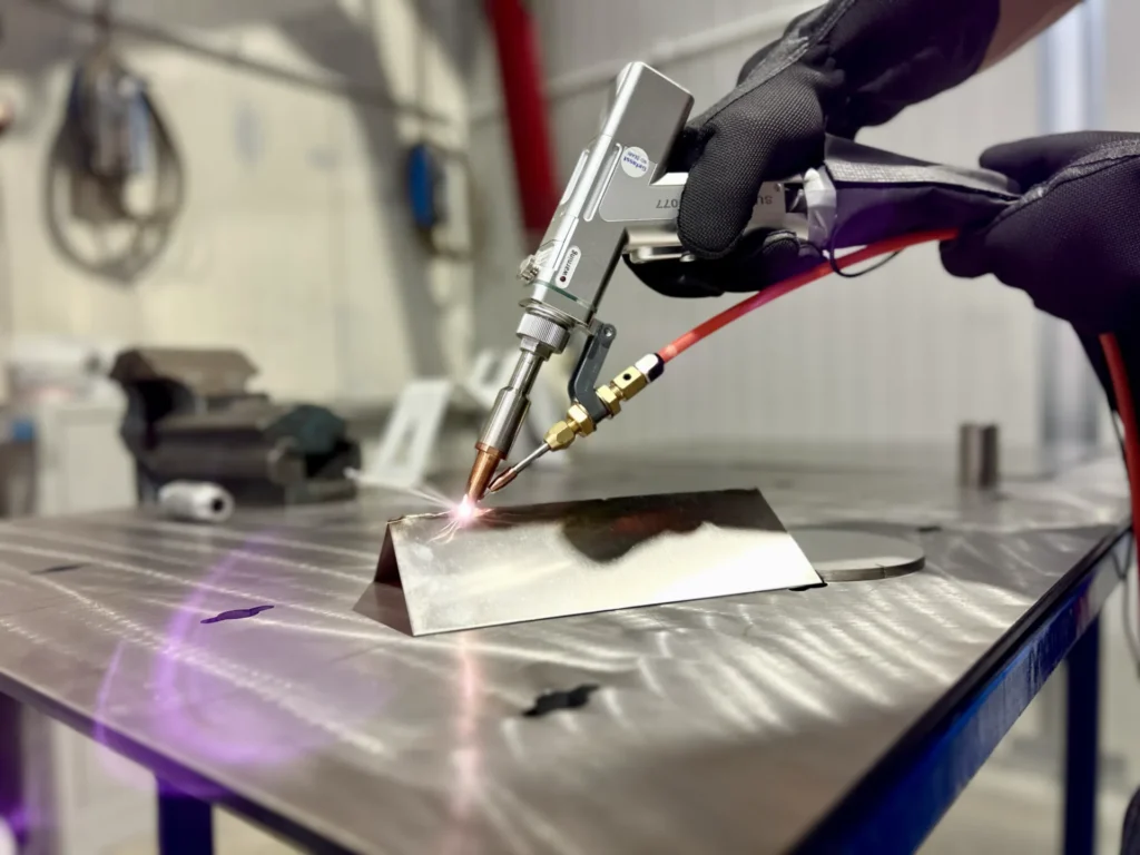primo piano con sfondo sfocato che mostra in evidenza la pistola della saldatrice laser 3 in 1 serie smart hwe, durante la saldatura di un pezzo in metallo